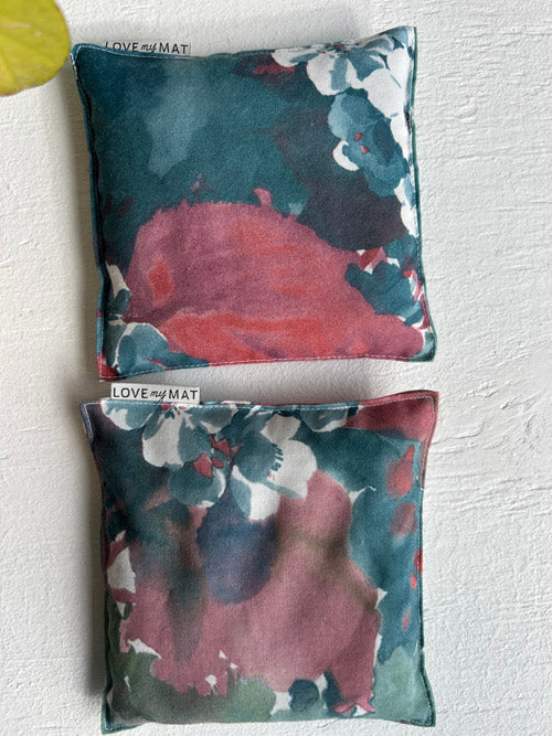 Two floral-patterned knee pillows on a textured white surface with 'LOVE AT FIRST MAT' branding.