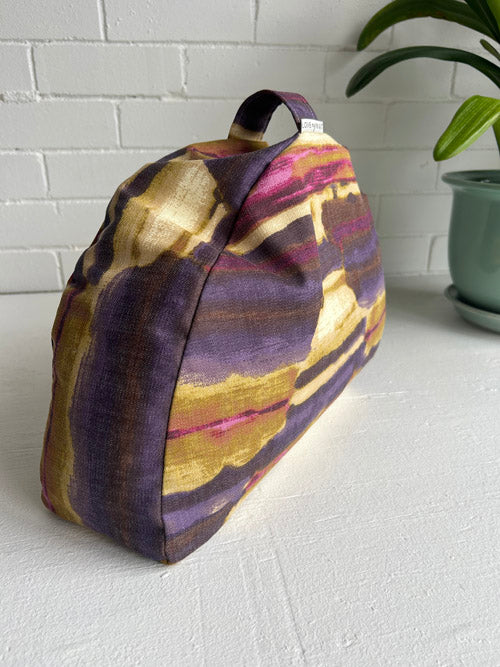 Colorful abstract fabric meditation cushion on a white surface with a plant in the background