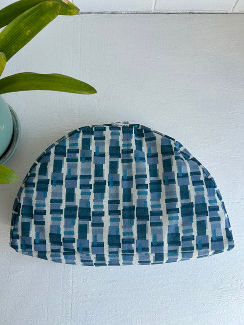 Blue and white checkered sit cushion on a light blue surface with a plant leaf in the corner.