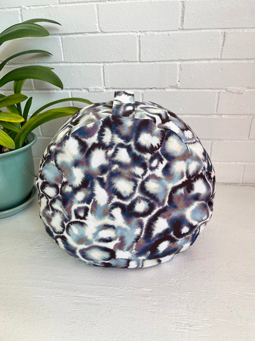 Round seat cushion with a pattern on a white surface next to a plant.