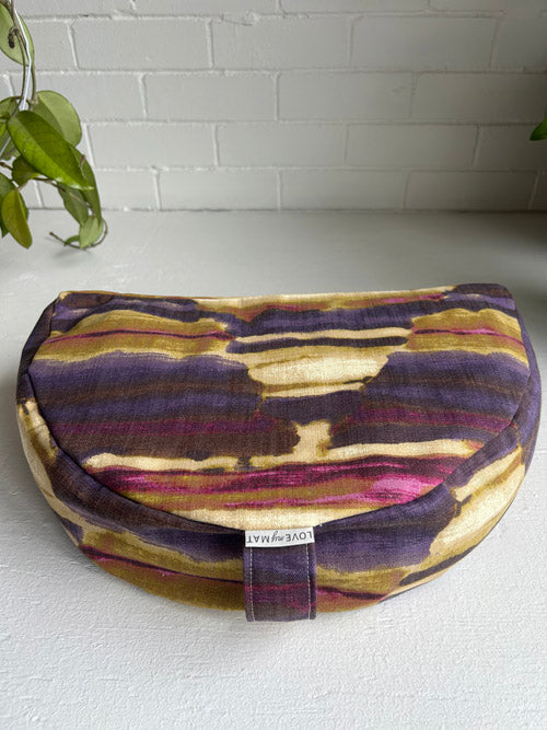 Multicolored abstract meditation cushion on a white surface with a plant in the background