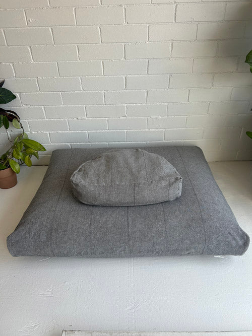 Gray meditation cushion on a white surface with a white brick wall in the background