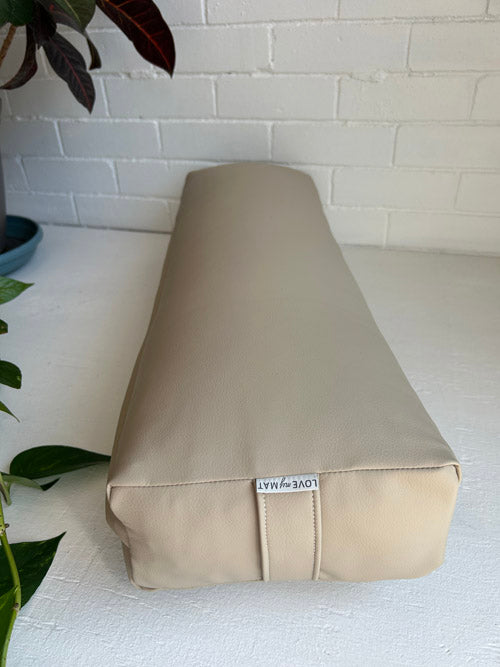 Beige yoga bolster with a visible brand label on a white surface with a white brick wall background.