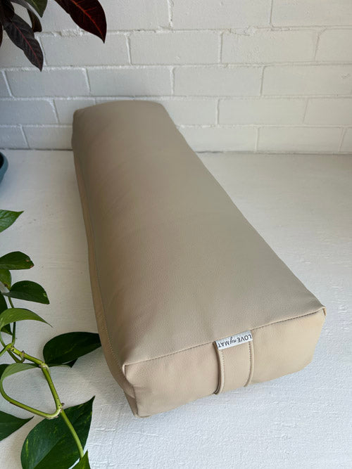 Beige vinyl long yoga bolster on a white surface with a plant in the foreground
