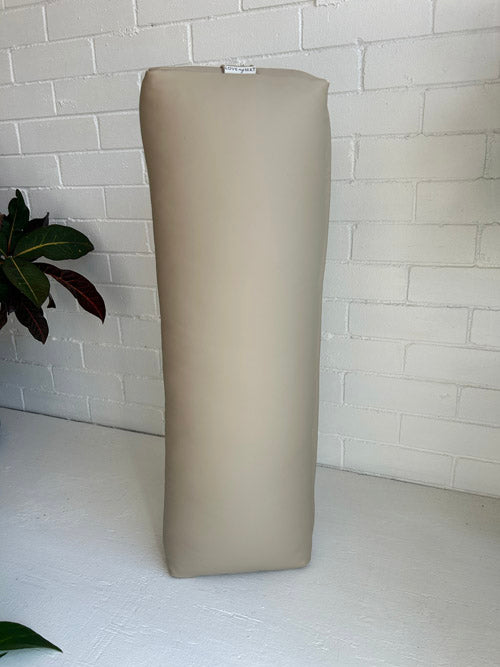 Beige Vinyl Yoga bolster against a white brick wall