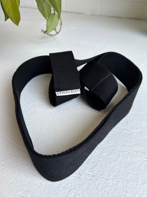 Black yoga strap on a white surface with a plant in the background