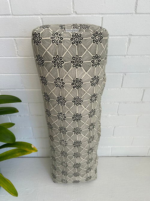 Black and cream print fabric yoga bolster  against a white tiled wall