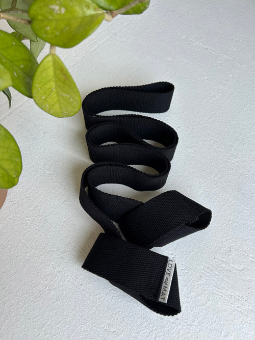 Black yoga starp on a light gray surface with green leaves in the corner