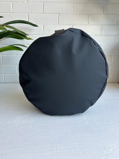 Black round bag on a white surface with a light gray brick wall background