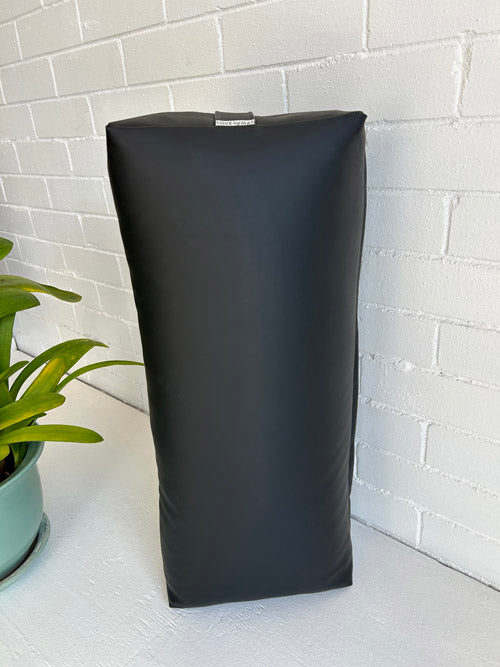 Black traditional yoga bolster on a white surface with a white brick wall background
