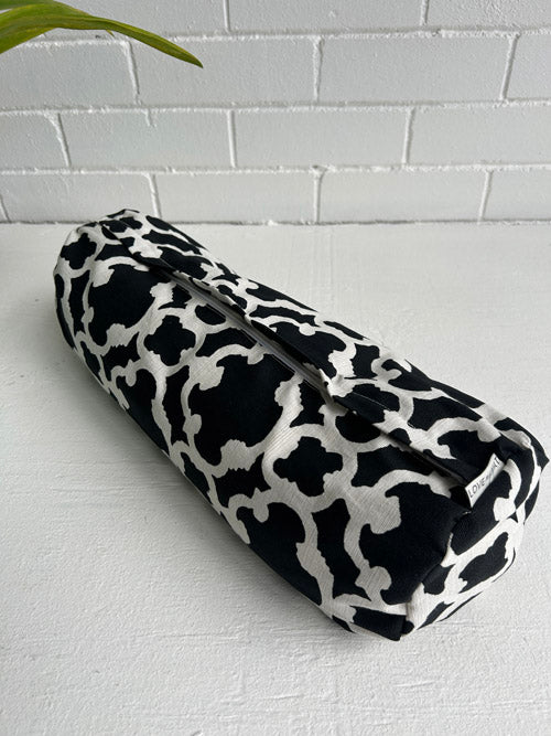 Black and white patterned mini yoga bolster on a light gray surface with a white tiled wall background.