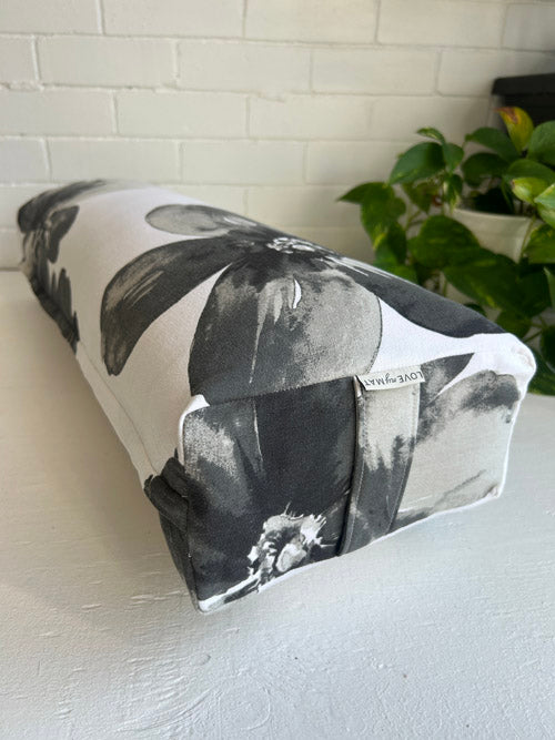 Floral-patterned long yoga bolster on a white surface with a plant in the background