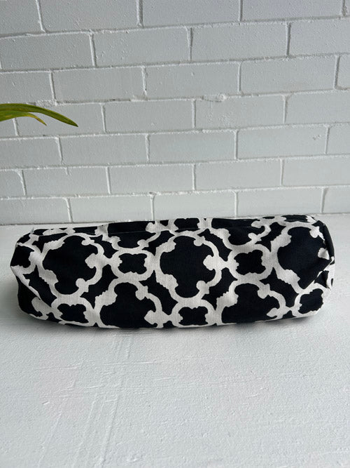 Black and white patterned small yoga bolster on a light gray surface with a light gray brick wall background.