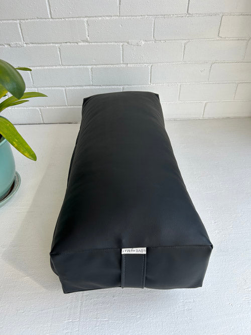 Black Canadian made Yoga Bolster on a white surface with a plant in the background