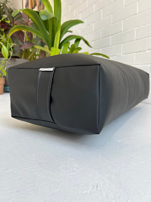 Black traditional yoga bolster on a light surface with plants in the background