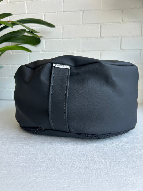 Black duffel bag on a light gray surface with a white brick wall background