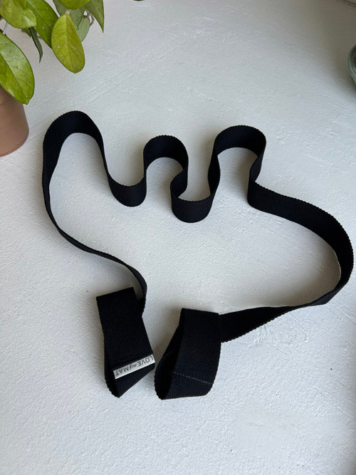 Black Yoga Strap on a light surface with a plant in the corner