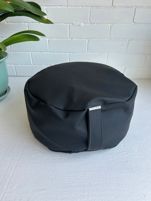 Black bean-shaped ottoman on a white surface with a light gray brick wall in the background.