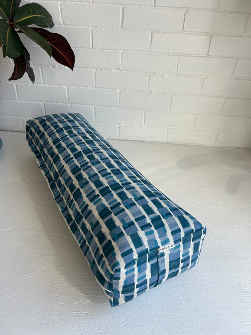 Rectangular blue and white long yoga bolster on a light surface with a white brick wall background