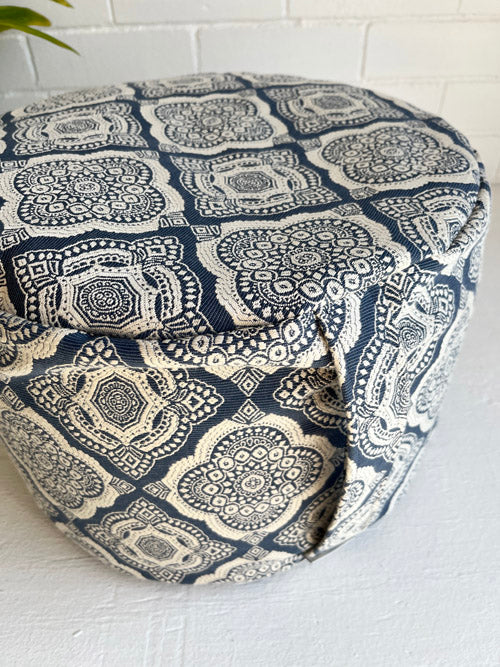 Blue and white patterned floor meditation cushion with a carry handle on a white surface with a tiled wall background