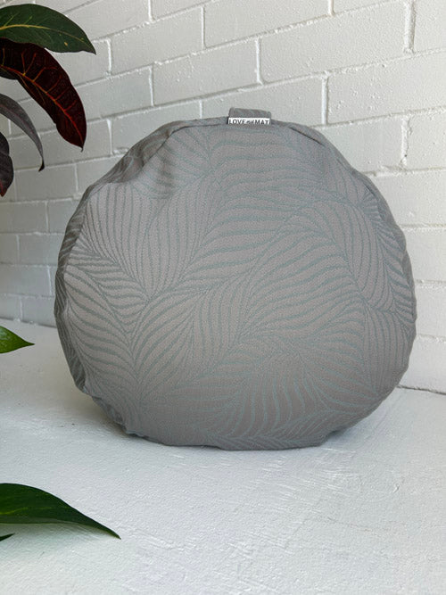 Gray textured meditation cushion on a white surface with a white brick wall background