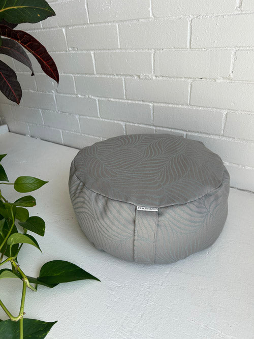 Gray textured grey meditation cushion on a white surface with a white brick wall background