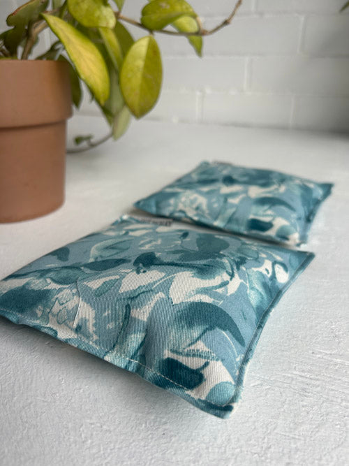 Two blue patterned knee pillows on a white surface with a plant in the background.