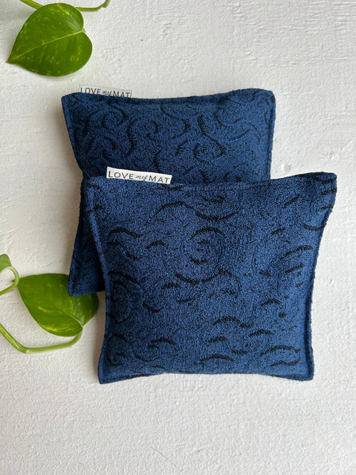 Two blue patterned yoga knee pillows on a light gray background with a green leaf.