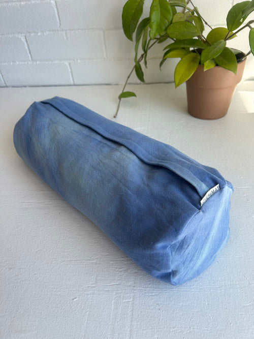 Blue cylindrical fabric yoga bolster on a white surface with a plant in the background