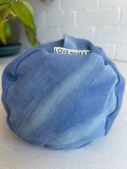 Blue fabric round yoga bolster with a label on a white surface
