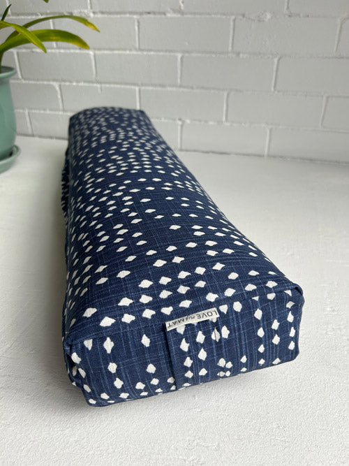 Blue and white patterned small yoga bolster on a white surface with a plant in the background