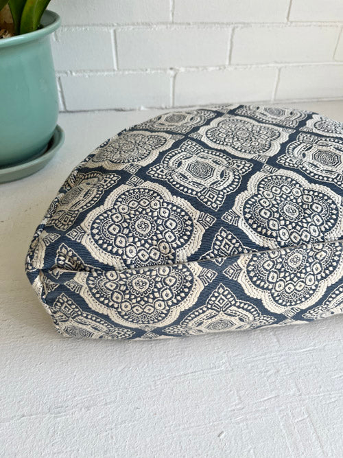 Blue and white patterned cushion on a white surface with a plant in the background