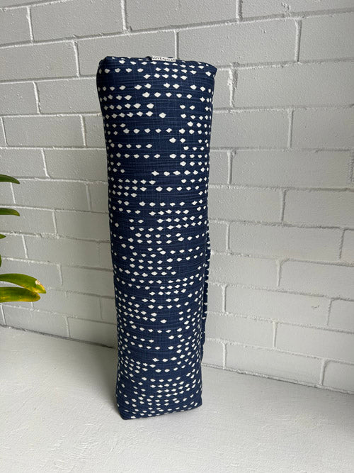 Blue fabric small Yoga Bolster with white pattern on a white surface against a white brick wall.