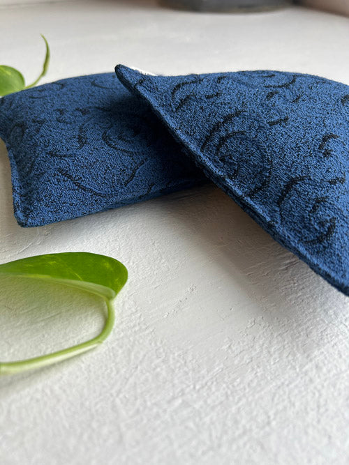 Two blue textured yoga knee pillows on a white surface with green leaves.