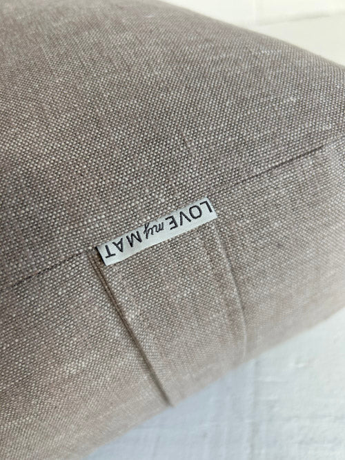 Taupe fabric yoga bolster with a label on a white background