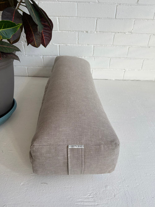 taupe fabric yoga bolster on a white surface with a plant in the background