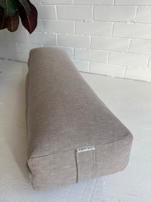 taupe fabric yoga bolster laying on white surface and white background