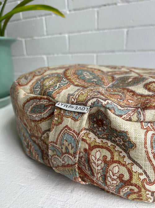 Paisley fabric close up of a meditation cushion  and 'LOVE THE MAT' tag on a white surface.