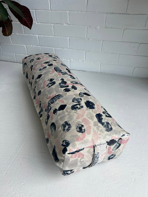 Long Yoga Bolster with abstract pattern on a white floor against a white brick wall.