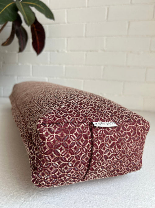 Geometric burgundy fabric yoga bolster on a white surface