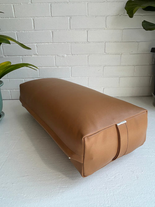 Brown yoga bolster on a white floor with a white brick wall background