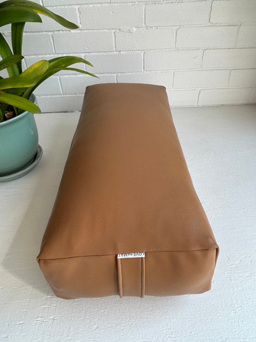 Brown Canada made yoga bolster on a white surface with a plant in the background