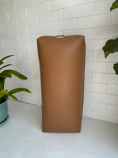 Brown Traditional Yoga Bolster on a white surface with a white brick wall background