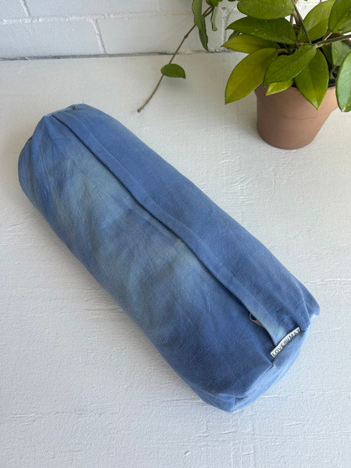 Blue cylindrical pillow on a white surface with a plant in the background