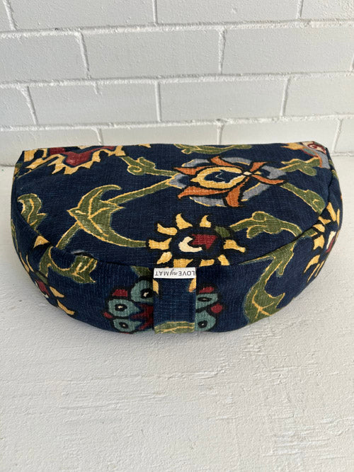 Fun high contrast floral fabric meditation cushion against a white brick wall and on a white surface.