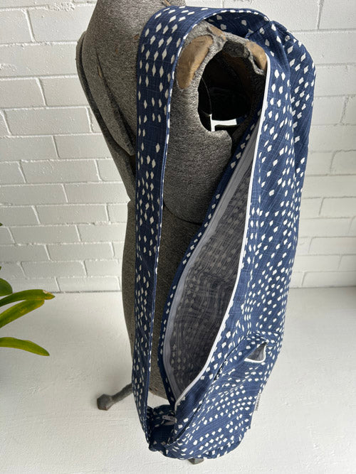 Blue patterned yoga mat carrier against a white brick wall.