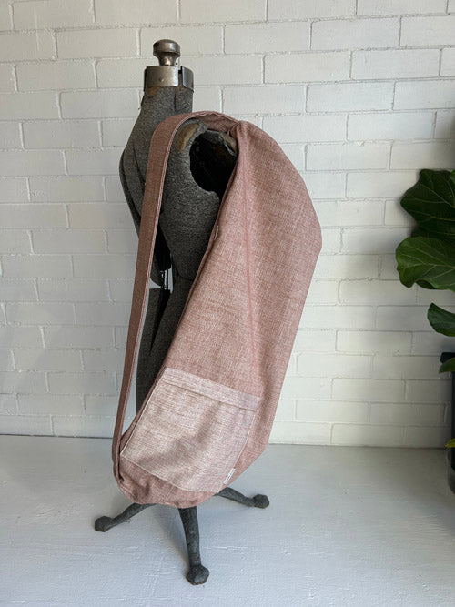 Dusty Pink yoga mat bag draped over a mannequin against a white brick wall.