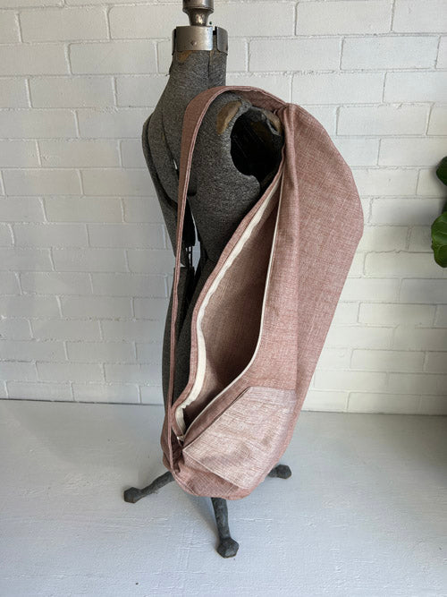 Brown/pink fabric yoga mat bag on a mannequin stand against a white tiled wall.