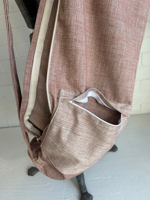 Brown/pink textured sling yoga mat bag with a pocket on a mannequin against a white brick wall.