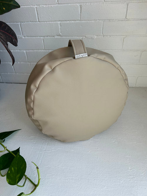 Round beige meditation cushion with a tag on a white surface and light gray brick wall background